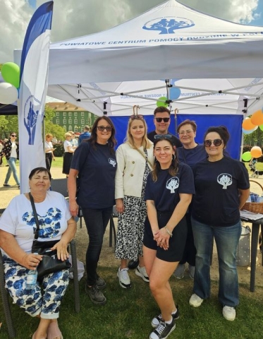 Grupa ludzi stojąca pod namiotem Powiatowego Centrum Pomocy Rodzinie w Policach