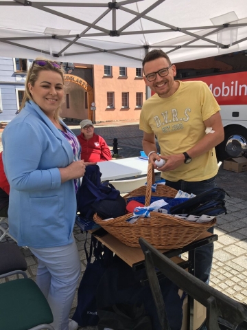 Dwie osoby stojące przy wiklinowym koszu, wybierajace upominek, w tle zabudowania mieszkalne