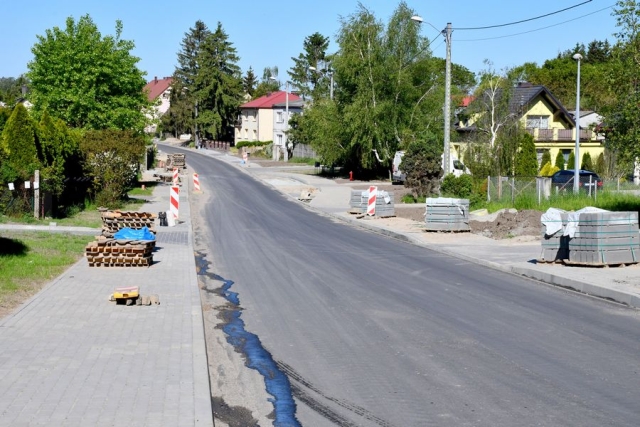 Remont drogi, trwają prace układania krawężników i chodników,w tle zabudowa mieszkalna, zielone drzewa i krzewy