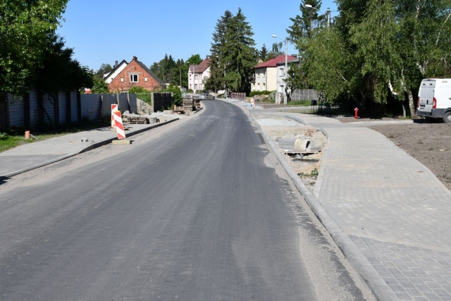 Remont drogi, trwają prace układania krawężników i chodników,w tle zabudowa mieszkalna, zielone drzewa i krzewy