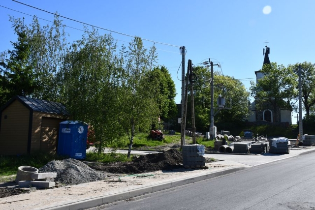 Remont drogi, trwają prace układania krawężników i chodników,w tle kościół, zielone drzewa i krzewy