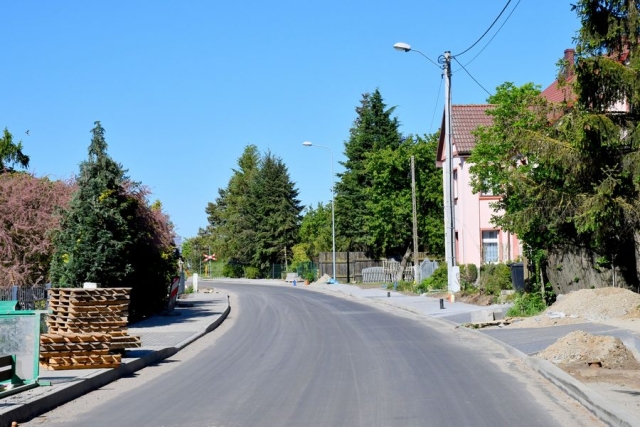 Remont drogi, trwają prace układania krawężników i chodników,w tle zabudowa mieszkalna, zielone drzewa i krzewy