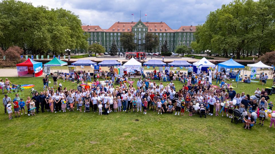 Uczestnicy festynu, dorośli i dzieci pozujący do grupowego zdjęcia na trawniku podczas pikniku.