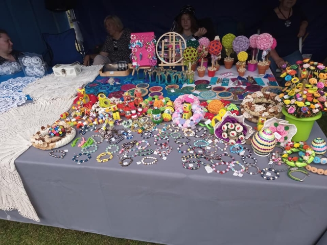 Stoisko z rękodziełem, na stole wyłożone ręcznie robione między innymi bransoletki, kwiaty, stroiki