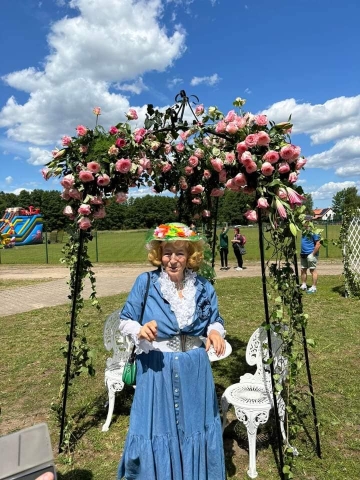 Kobieta w kolorowej sukience i kapeluszu, stojąca pod różaną bramą