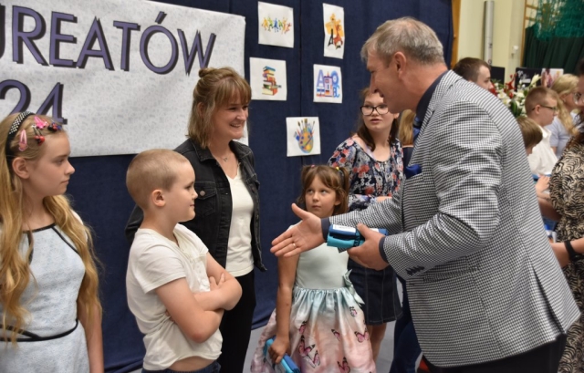 Członek Zarządu Powiatu w Policach Jacek Fabisiak podaje rękę oraz upominek składając gratulacje dla uczniów