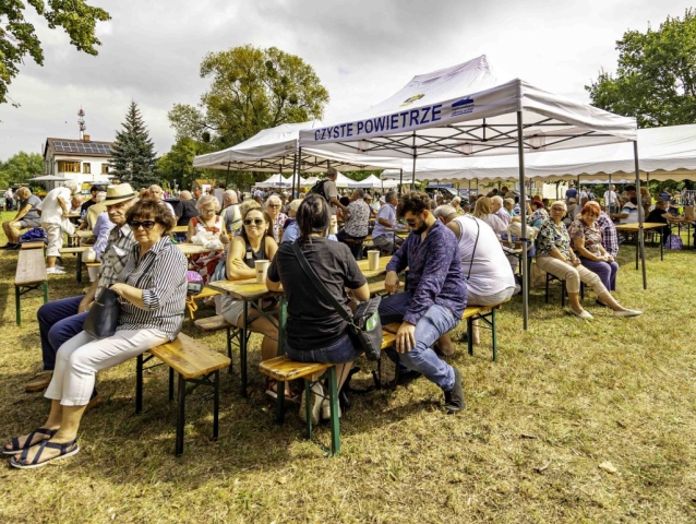 Uczestnicy wydarzenia siedzący przy drewnianych stolikach